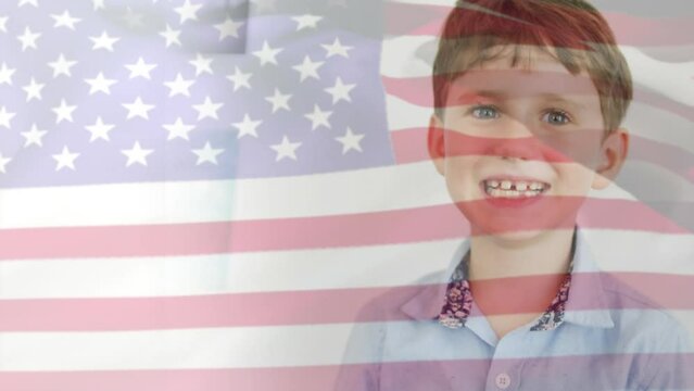 Animation of american flag blowing over happy caucasian schoolboy smiling in classroom