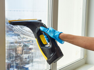 Close-up of a woman's hand cleaning a window with a professional vacuum cleaner