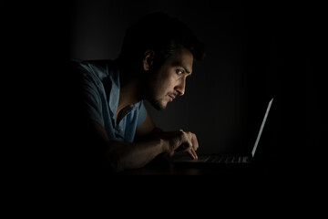Side view of young handsome man working on laptop at night. Work from home concept	