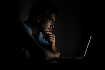 Side view of young handsome man working on laptop at night. Work from home concept	