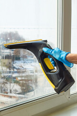 gloved hand cleans a window with a professional vacuum cleaner