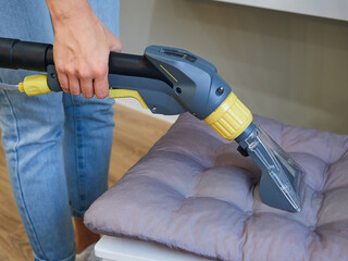 Close-up woman cleaning cushions on a chair using a vacuum cleaner