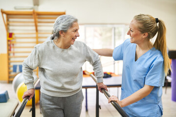 Physiotherapist assisting elderly woman in movement therapy at rehab center
