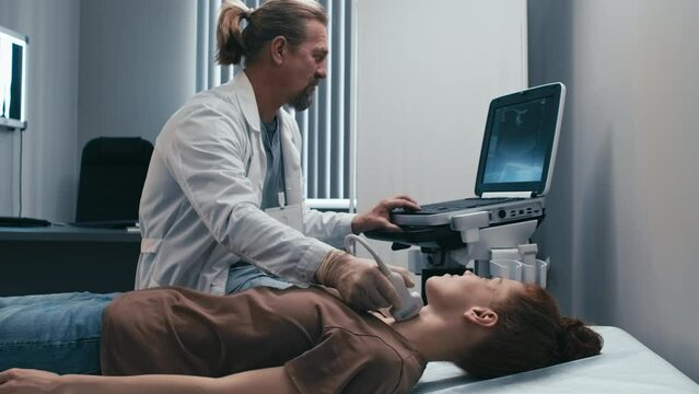 Modern mature Caucasian medical specialist doing thyroid sonography for young female patient