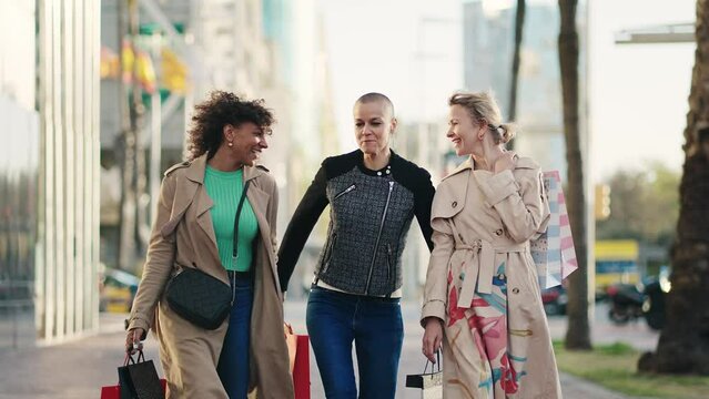 Three happy women friends with shopping bags walking on street in the city for Spring sales