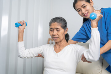 Young pretty asian physiotherapist helping senior female patient holding dumbbell in physical therapy session, concept of World Confederation for Physical Therapy.