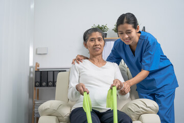 Fototapeta premium Concept of World Confederation for Physical Therapy. young physiotherapist caregiver helping mature elderly woman training with elastics in rehabilitation center, muscle weakness
