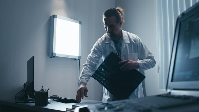 Mature Caucasian surgeon wearing white coat standing in his office reading patients X-ray pictures