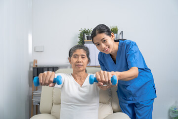 Fototapeta premium Young pretty asian physiotherapist helping senior female patient holding dumbbell in physical therapy session, concept of World Confederation for Physical Therapy.