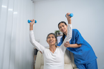 Young pretty asian physiotherapist helping senior female patient holding dumbbell in physical therapy session, concept of World Confederation for Physical Therapy.