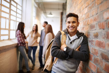 Education, arms crossed and portrait of man in school hallway for studying, college and scholarship. Future, happy and knowledge with student leaning on brick wall for university, academy and campus