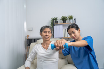Obraz premium Young pretty asian physiotherapist helping senior female patient holding dumbbell in physical therapy session, concept of World Confederation for Physical Therapy.