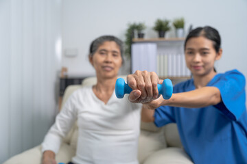 Young pretty asian physiotherapist helping senior female patient holding dumbbell in physical therapy session, concept of World Confederation for Physical Therapy.