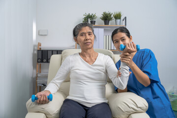 Young pretty asian physiotherapist helping senior female patient holding dumbbell in physical therapy session, concept of World Confederation for Physical Therapy.