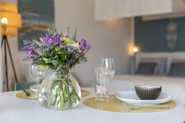 Detail of a place set for lunch, with a plate, cutlery and a glass. There is a bouquet of fresh flowers