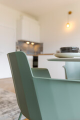 Detail of turquoise chair and white table with dishes on it. The kitchen is in the background
