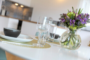 Detail of a place set for lunch, with a plate, cutlery and a glass. There is a bouquet of fresh flowers
