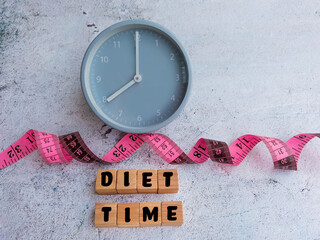 Pink measuring type , alarm clock and diet time message on wooden blocks . Diet concept .Eating...
