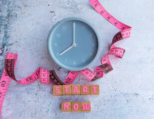 Pink measuring type , alarm clock and start now message on wooden blocks . Diet concept .Eating...