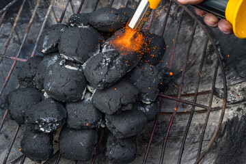 Brykiet węgla drzewnego rozpalany w grillu palnikiem gazowym z którego wydobywa się pomarańczowo-czerwony płomień i iskry