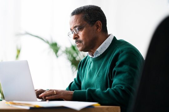 Concentrated Ethiopian male entrepreneur with laptop looking at screen and analyzing data while sitting at desk and working on project in spacious workplace