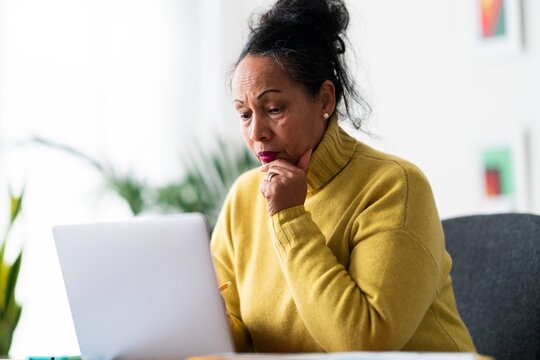 From below of attentive aged Ethiopian female self employed looking at screen and analyzing statistics while creating project and working online with portable laptop