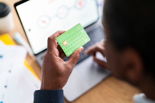 Soft focus of crop unrecognizable Ethiopian male client with portable computer buying and making payment with card while sitting at desk and shopping online