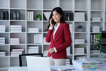 Image of a young Asian woman talking on a smartphone while working in an office