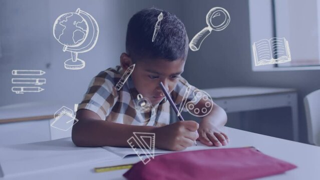 Animation of school icons over biracial schoolboy concentrating writing at desk in class