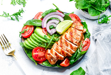 Healthy vegetable salad with grilled chicken fillet, spinach, tomatoes, avocado and onion with olive oil on white table background. Tasty detox, ketogenic diet food. Top view