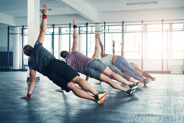 Fitness, group class and athletes doing a exercise in the gym for health, wellness and flexibility. Sports, training and people doing side plank exercise challenge together in sport studio or center.