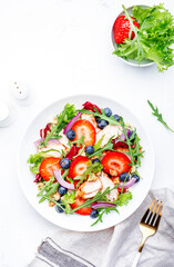 Summer strawberry and grilled chicken healthy salad with arugula, blueberries, red onion and walnuts, white table. Fresh useful dish for healthy eating