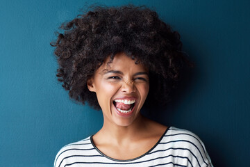 Portrait, funny and woman with tongue out, silly and happiness against a blue studio background. Face, female person and model with facial expression, humor and comic with joy, smile and goofy girl - obrazy, fototapety, plakaty