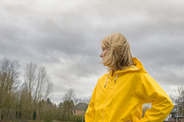 A young woman in a yellow raincoat looks up at the stormy sky. Waiting for rain. European landscape in bad weather