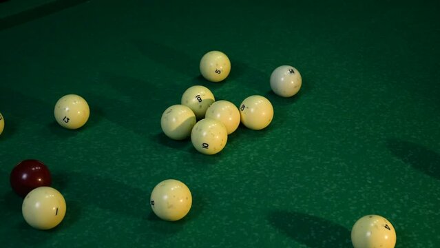 White billiard balls are folded into a triangle by male hands. On a green billiard table, the balls are collected into a triangle pyramid and pushed to the edge. The concept of Russian billiards.