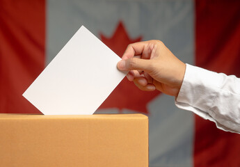 Hand voter holding ballot paper putting into the voting box at place election against the Canada...