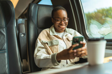 One woman, beautiful young lady riding in train, using mobile phone. African-American young woman...