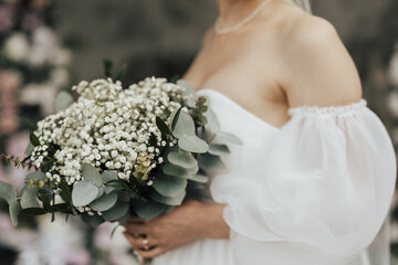 Cropped shot of bride while is holding a wedding classic bouquet in her hands. Bridal accessories. Close-up of bunch of white flowers.	