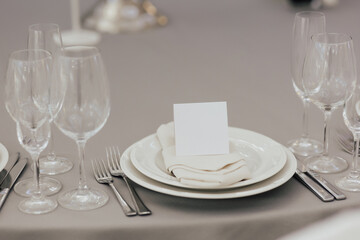Table for guests, covered with a gray tablecloth served with cutlery, plate and glasses.	