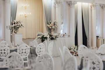 Tables setting up for wedding. Interior of restaurant for wedding dinner, ready for guests. Decorated with floral arrangement. Dishes, wine glasses and napkins.