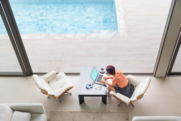 Happy working senior digital nomad woman sitting with laptop at luxury pool villa near beach, Phuket Thailand.