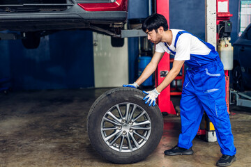 Professional car technician mechanic man in uniform work and maintenance repairing checking removing black wheel tire car before a long travel in auto service.Automobile service garage