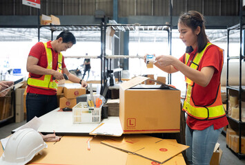 Warehouse staff packing goods for shipping order dispatch. Asian woman and colleague working in storehouse sealing cardboard box for shipment delivery. Logistics supply chain distribution management.