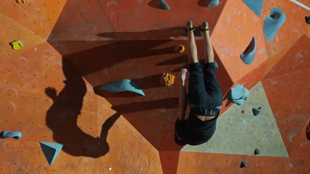 A young male office worker after work does sports in a climbing gym. A male climber hangs upside down on his feet during a workout in a gym on artificial rocks. High quality 4k footage