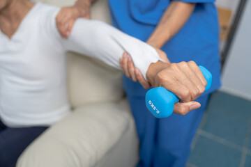 Young pretty asian physiotherapist helping senior female patient holding dumbbell in physical therapy session, concept of World Confederation for Physical Therapy.