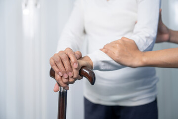 Attentive practitioner nurse assisting physical therapy elderly woman on a walking wood standard cane in disability nursing rehabilitation center, physical therapy encourage hands.
