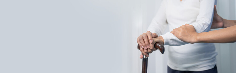 Attentive practitioner nurse assisting physical therapy elderly woman on a walking wood standard cane in disability nursing rehabilitation center, physical therapy encourage hands.