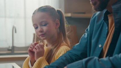 Caucasian happy family breakfast dinner at kitchen little cute child girl daughter eat bite eating crispy tasty bread with dad father cut baguette enjoying food delivery together at home childcare