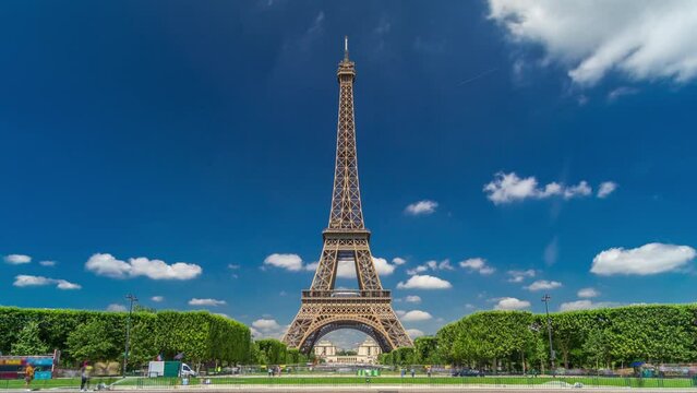 Eiffel Tower on Champs de Mars in Paris timelapse hyperlapse, France. Blue cloudy sky at summer day with green lawn and fountain with traffic around