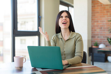 pretty young woman screaming with hands up in the air. laptop and desk concept